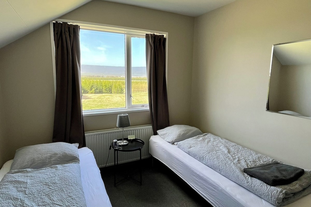 A room with two single beds, a small table, and a window with curtains.