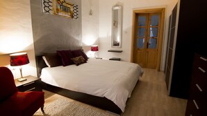 Ein Schlafzimmer mit einem Bett, einem roten Sessel, einem Nachttisch mit Lampe, einem Spiegel und einem Kleiderschrank.