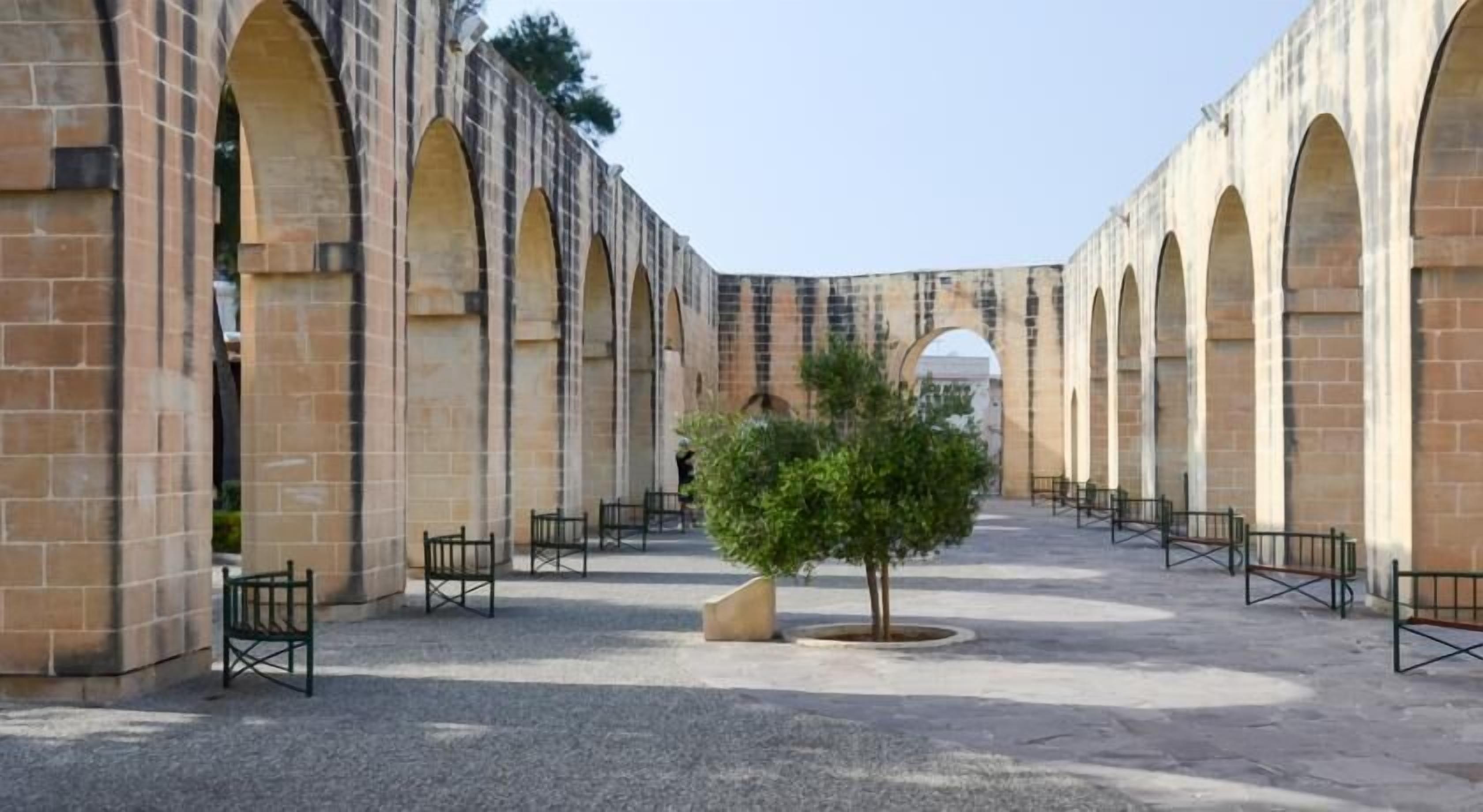 A courtyard with a central tree, surrounded by stone arches and benches.