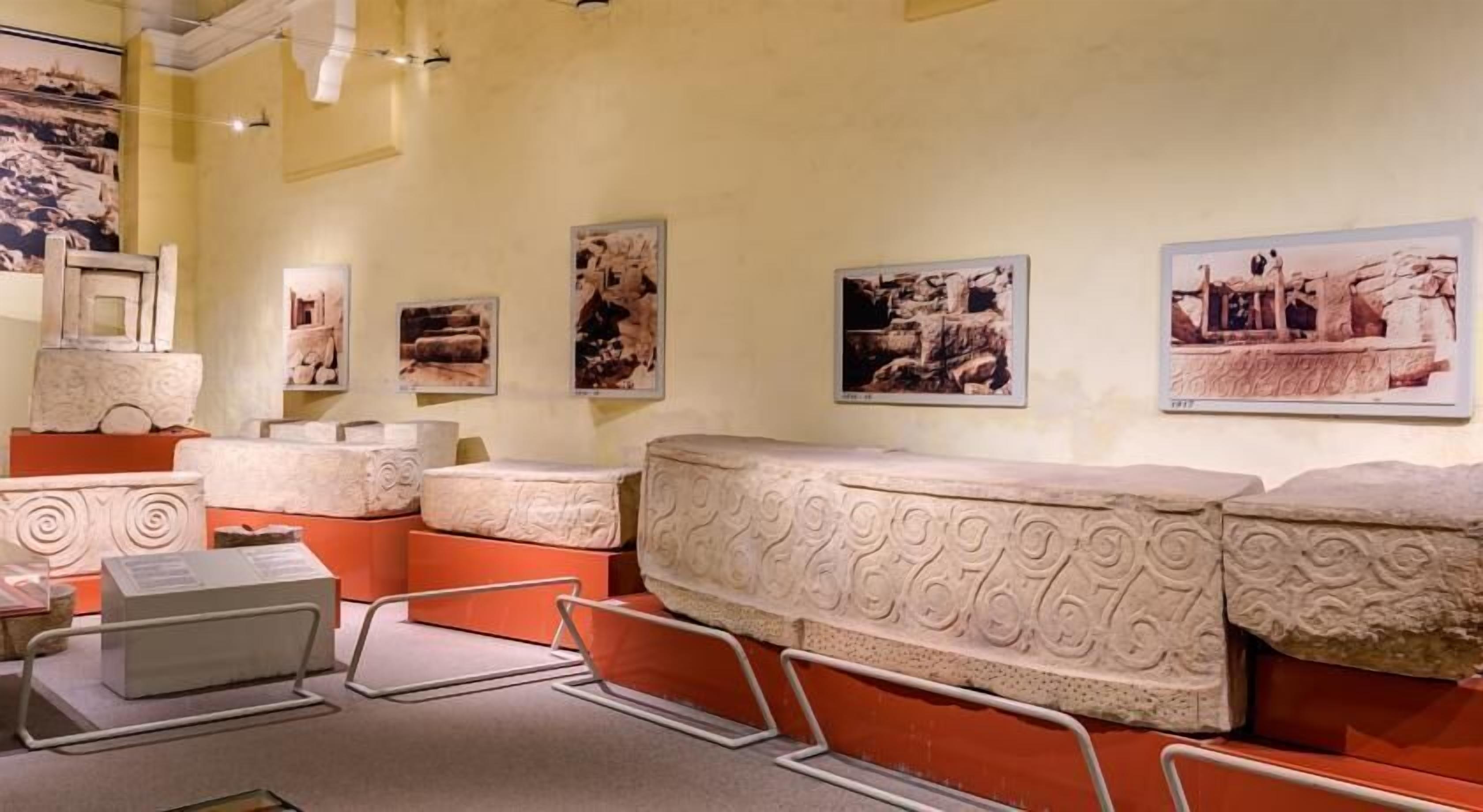 L’intérieur d’un musée, avec des sculptures en pierre, des panneaux d’information et des photographies accrochées aux murs.