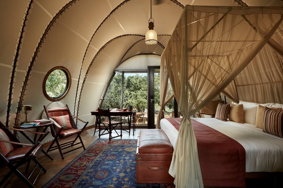 Un dormitorio con cama con dosel, una mesa redonda, dos sillas y vistas al exterior.