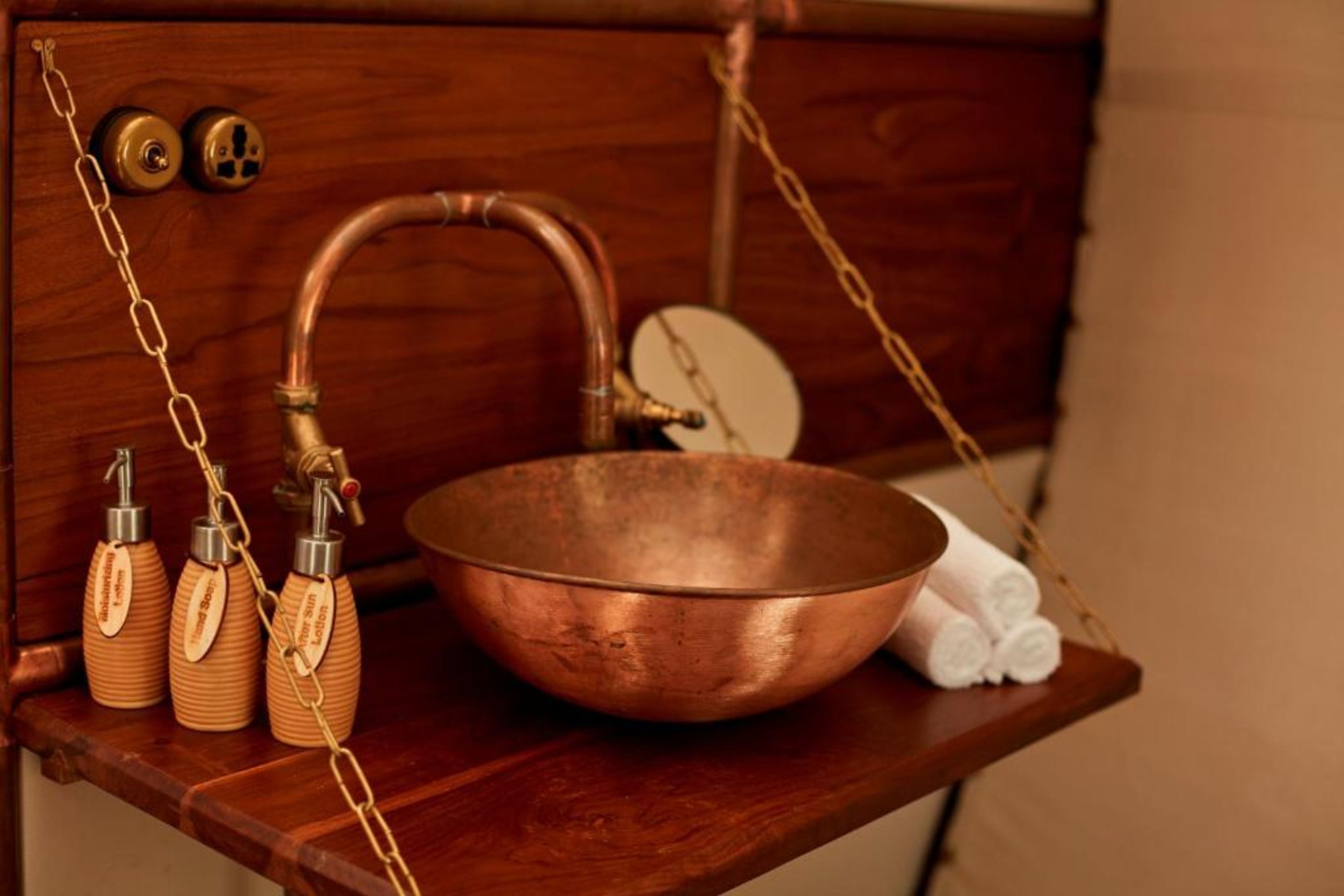 Un récipient en cuivre posé sur une étagère en bois, avec un porte-serviettes en bois et deux bouteilles en bois portant des étiquettes.