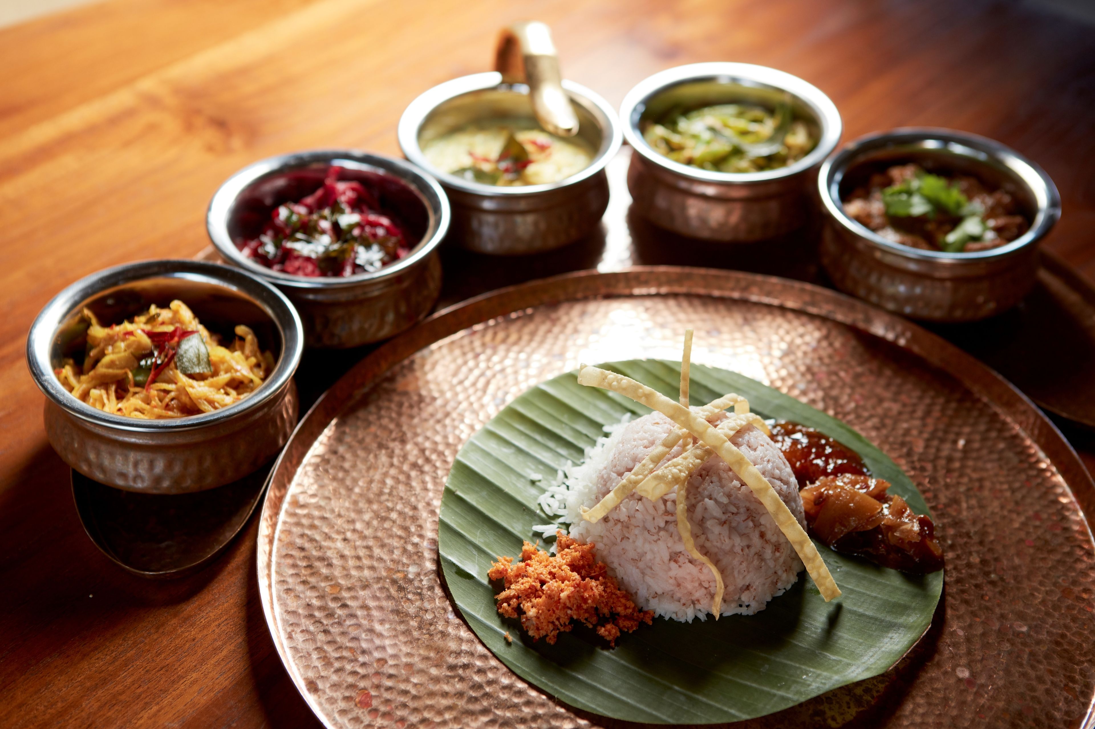 A traditional meal with rice, curry, and various side dishes served on a copper plate.