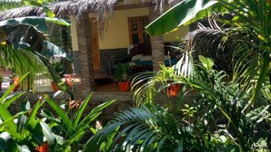 A small, thatched-roof house with a porch, surrounded by lush tropical plants. - Orchard Fruit Farm Bungalow (Phu Quoc)