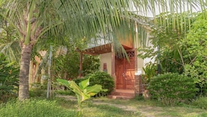 A bungalow with a wooden porch, surrounded by lush greenery and a palm tree. - Orchard Fruit Farm Bungalow (Phu Quoc)