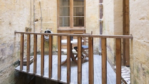 Un balcón de madera con una mesa, sillas, una ventana y una puerta.