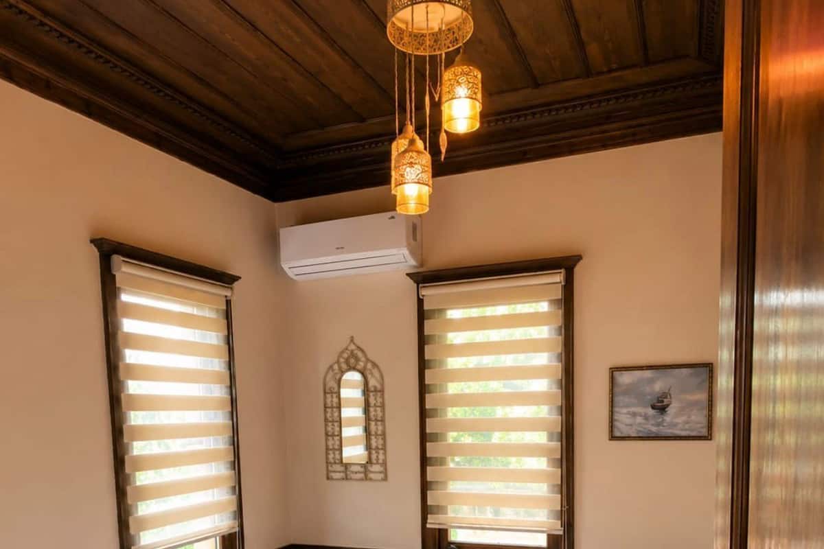 Un dormitorio con cama de madera, dos ventanas con persianas, un radiador y una lámpara colgante.