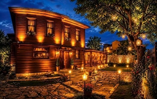 A wooden house with a stone pathway, potted plants, and outdoor lighting.