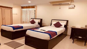 A hotel room with two beds, a desk, and an air conditioning unit. - Khyathi Hotels (Hyderabad)