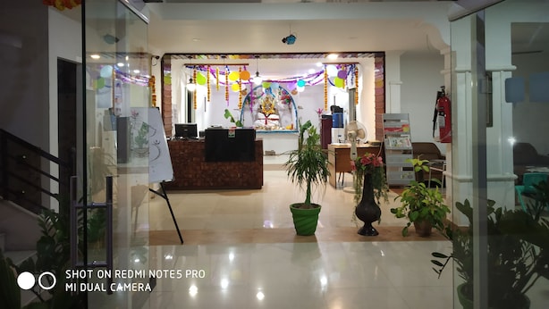 A reception area with a glass partition, a reception desk, a potted plant, and a fire extinguisher. - Khyathi Hotels (Hyderabad)