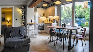 Uma sala de estar acolhedora com um sofá, um espaço de jantar com mesa e cadeiras, uma cozinha com eletrodomésticos modernos e uma grande janela com vista para o exterior.