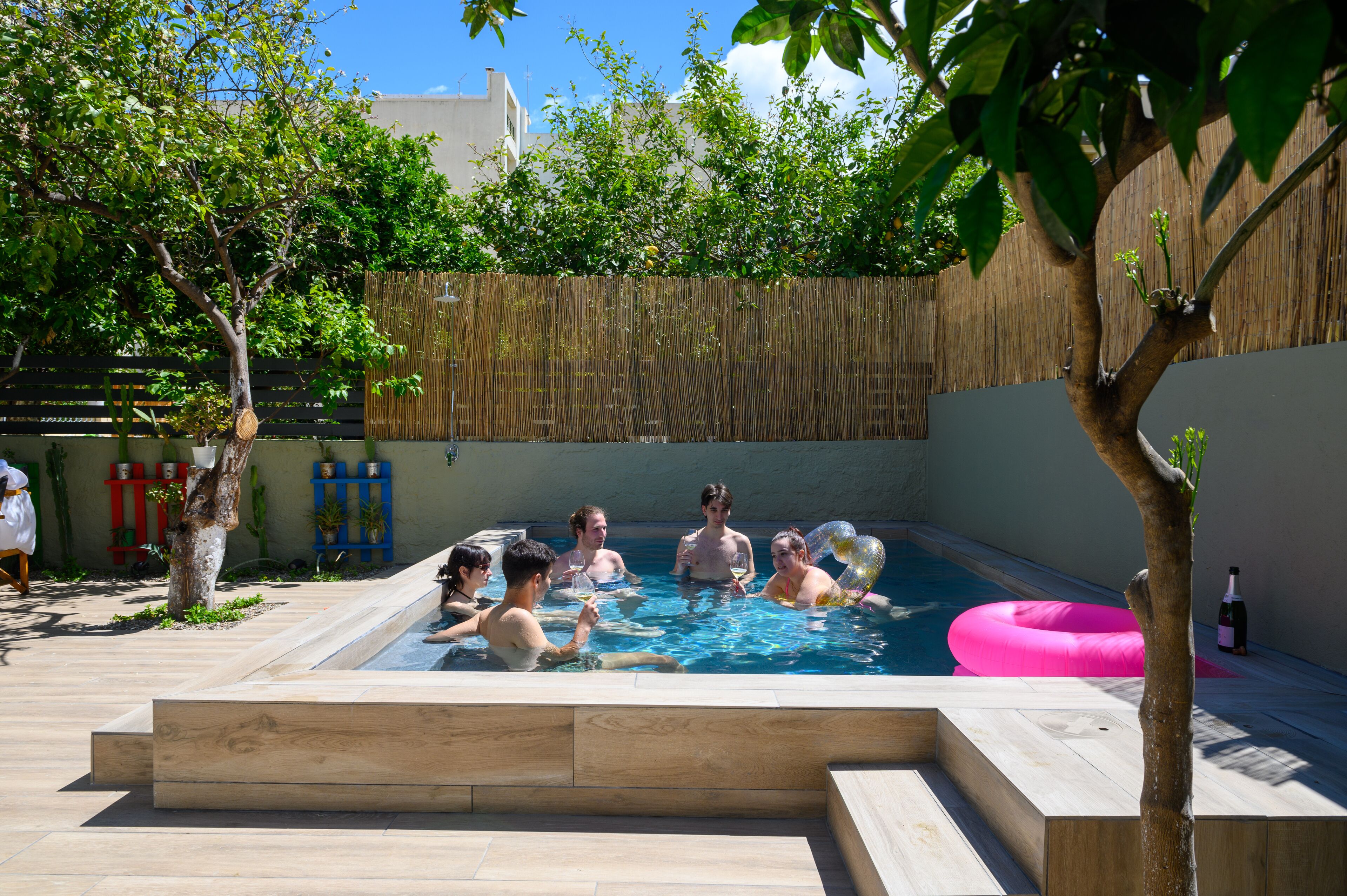A swimming pool area with a bamboo fence, potted plants, and a wooden deck.