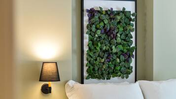 Uma obra de arte botânica emoldurada, uma luminária de parede e uma cama com roupa de cama branca.