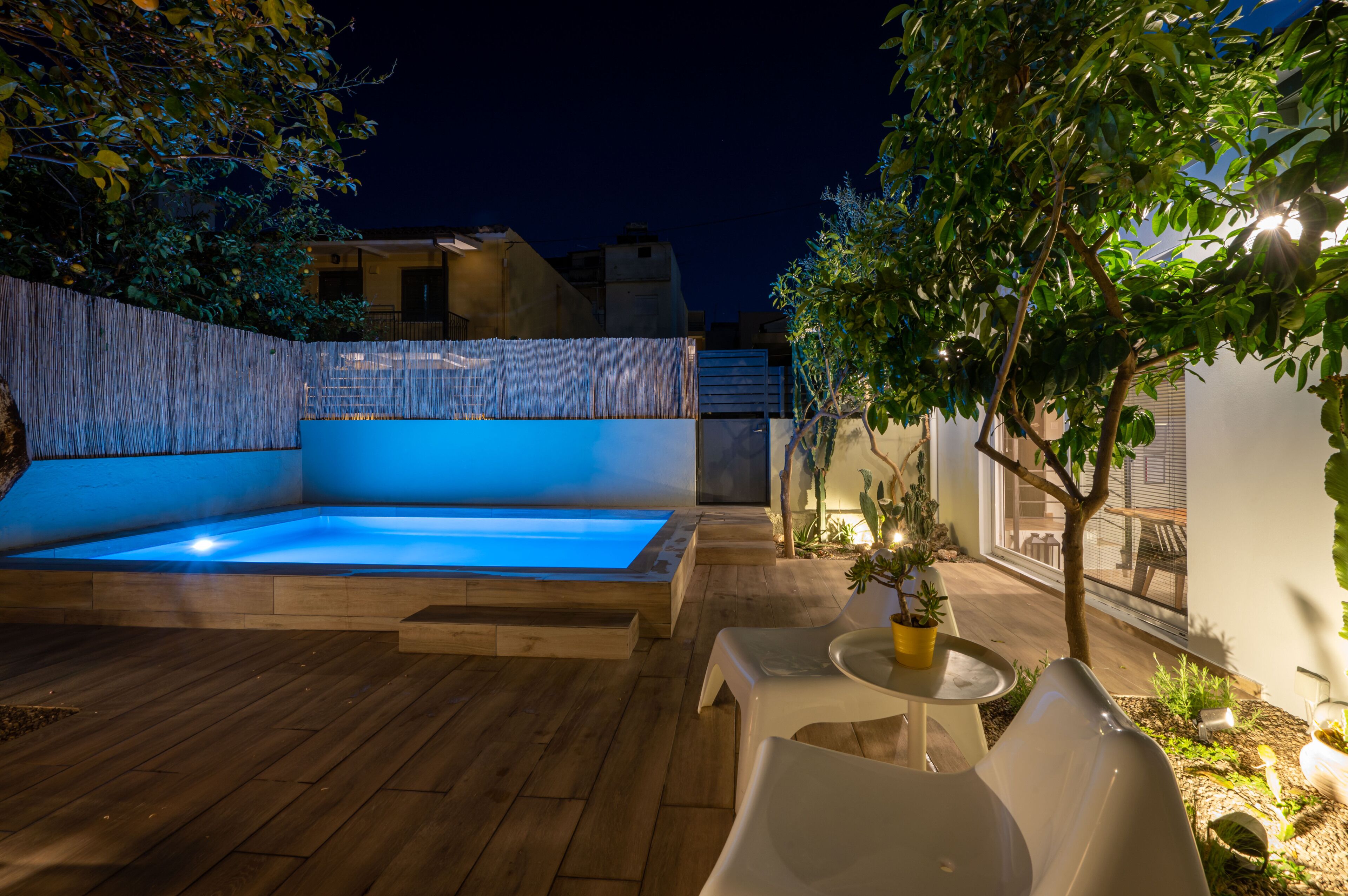 Un espace piscine extérieur moderne, doté d’une terrasse en bois, d’un coin salon intégré et de plantes en pot.
