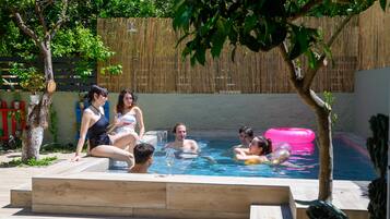 A swimming pool area with a bamboo fence, potted plants, and a wooden deck.