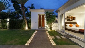 A modern house with a well-maintained lawn, a stone pathway leading to the entrance, and a bedroom with a large bed and a nightstand. - Luxury Pool Villa 608 (Pattaya)