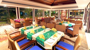 A restaurant with multiple tables set for dining, large windows, and a ceiling with wooden beams. - Ramya Resort & Spa (Udaipur)