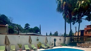 A swimming pool with a curved edge, surrounded by lounge chairs and umbrellas, with a clear blue sky above. - Carikci Hotel - + 16 Adult"s Only  (Marmaris)
