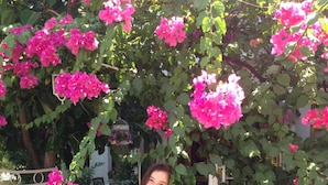 A woman holding pink flowers in front of a garden with potted plants and a white fence. - Carikci Hotel - + 16 Adult"s Only  (Marmaris)