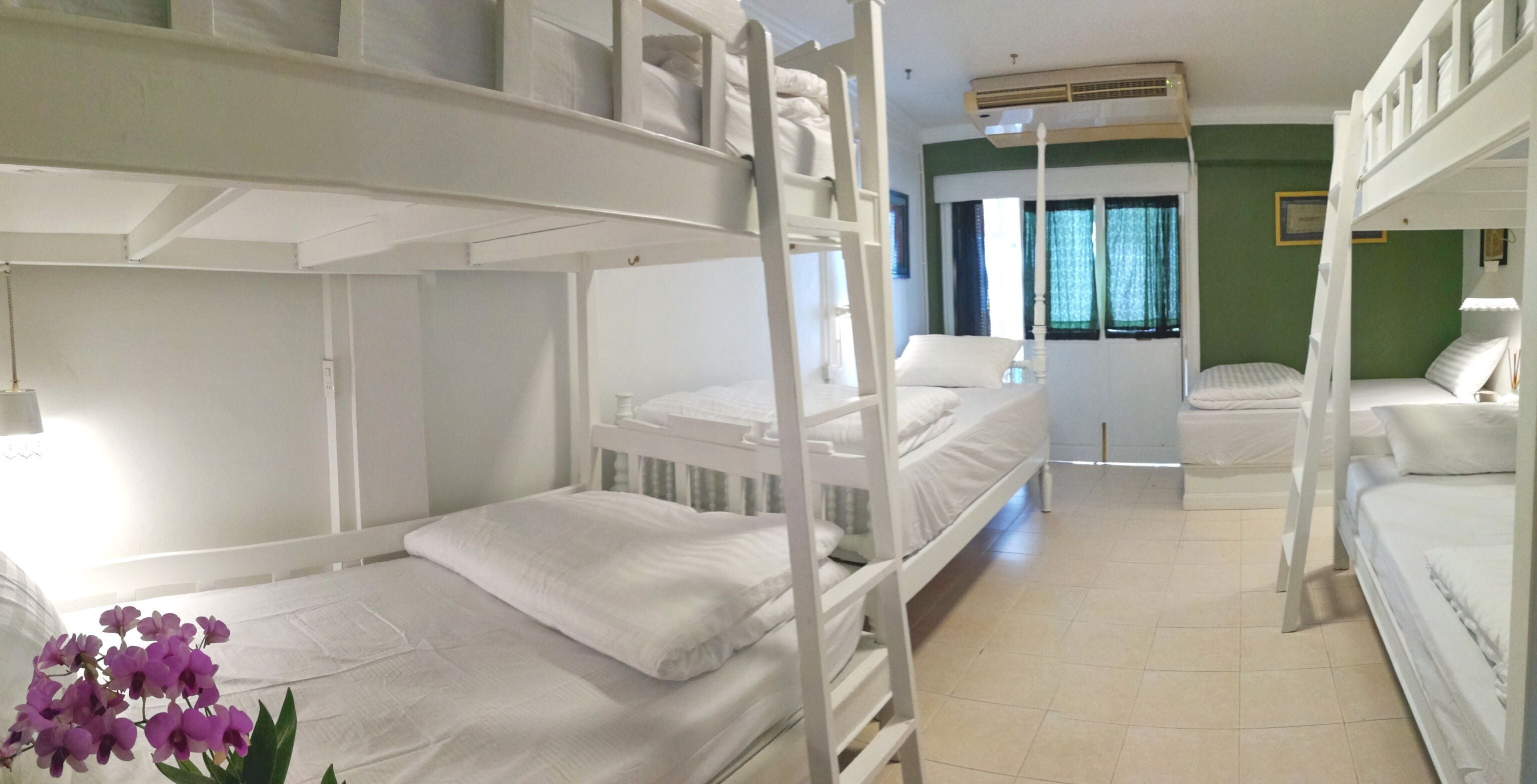 A bunk bed room with white bedding and a ladder, a window with curtains, and an air conditioning unit on the wall.