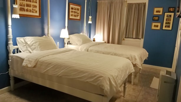 Een kamer met twee bedden, een raam met gordijnen en ingelijste foto's aan de muur.
