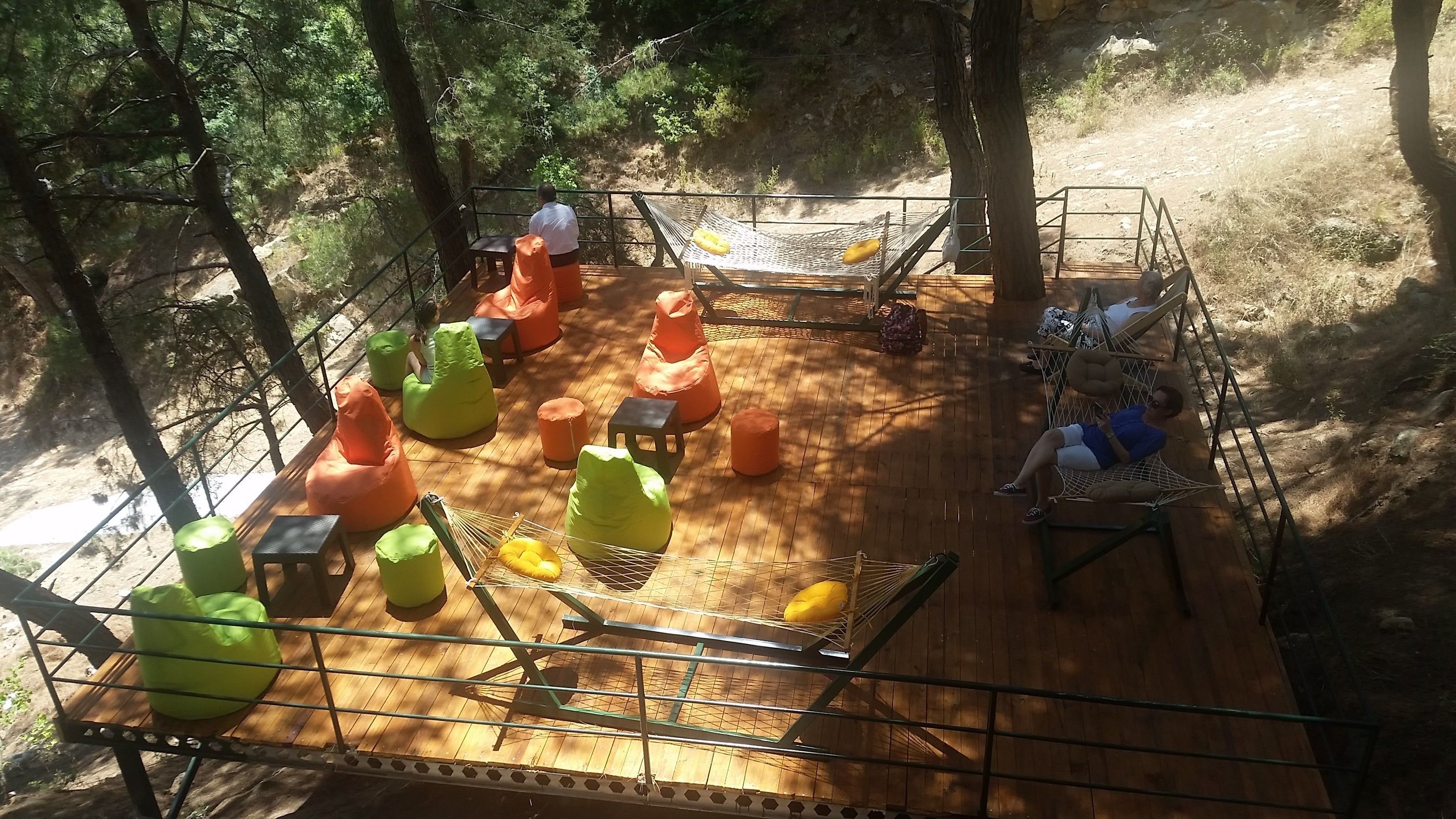 Eine Holzterrasse mit Sitzgelegenheiten, darunter Sitzsäcke und Hängematten, umgeben von Bäumen.