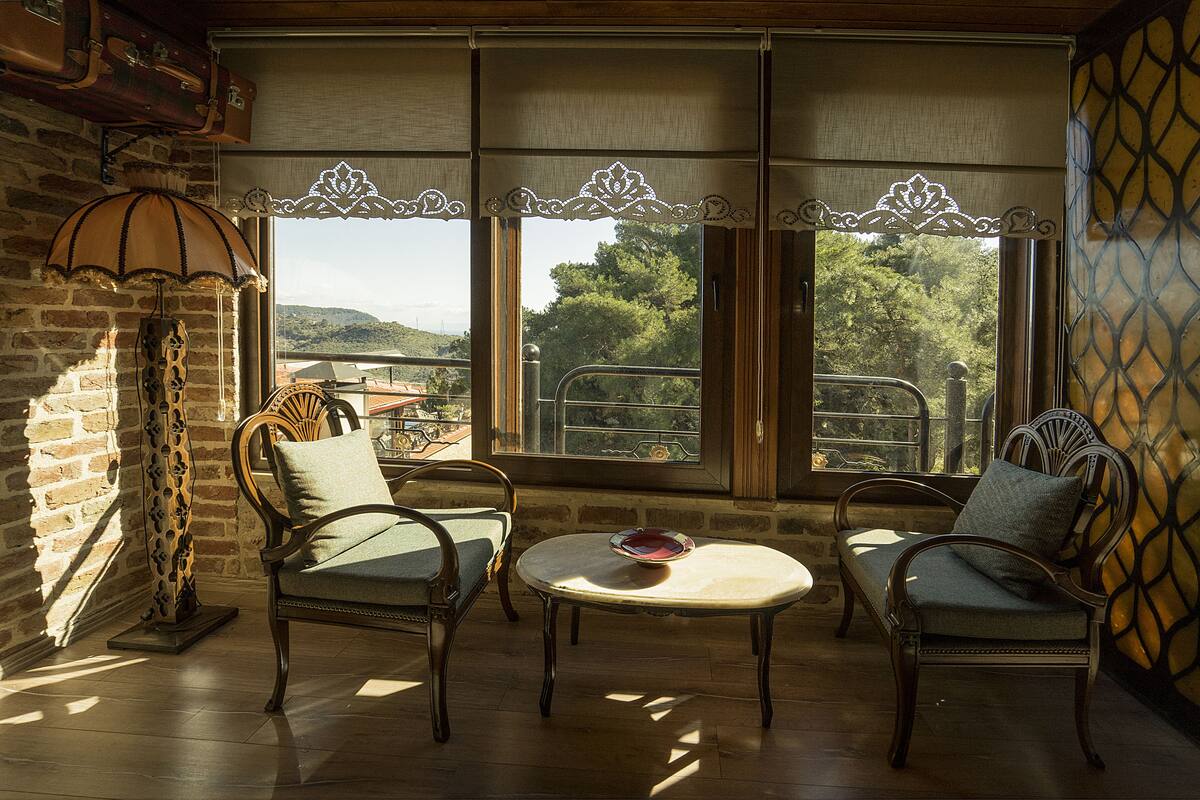 Una habitació acollidora amb dues cadires, una taula petita i vista cap a l'exterior a través de grans finestres.