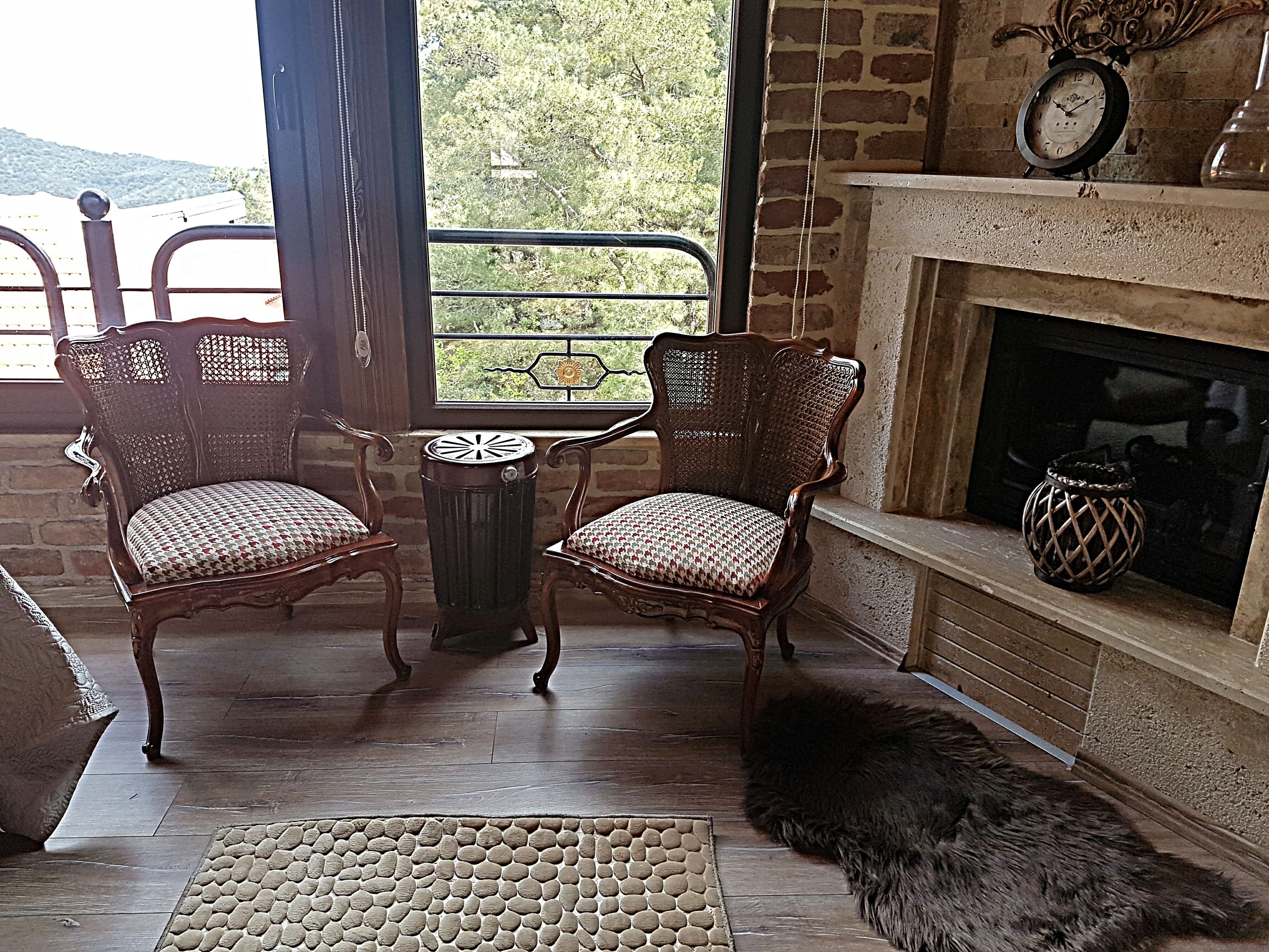 A cozy room with two wooden chairs, a small table, a fireplace, and a view of the outdoors.