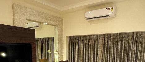 Una habitación de hotel con una cama grande, un televisor de pantalla plana, un escritorio con una silla, una mesita y un ventanal con cortinas.