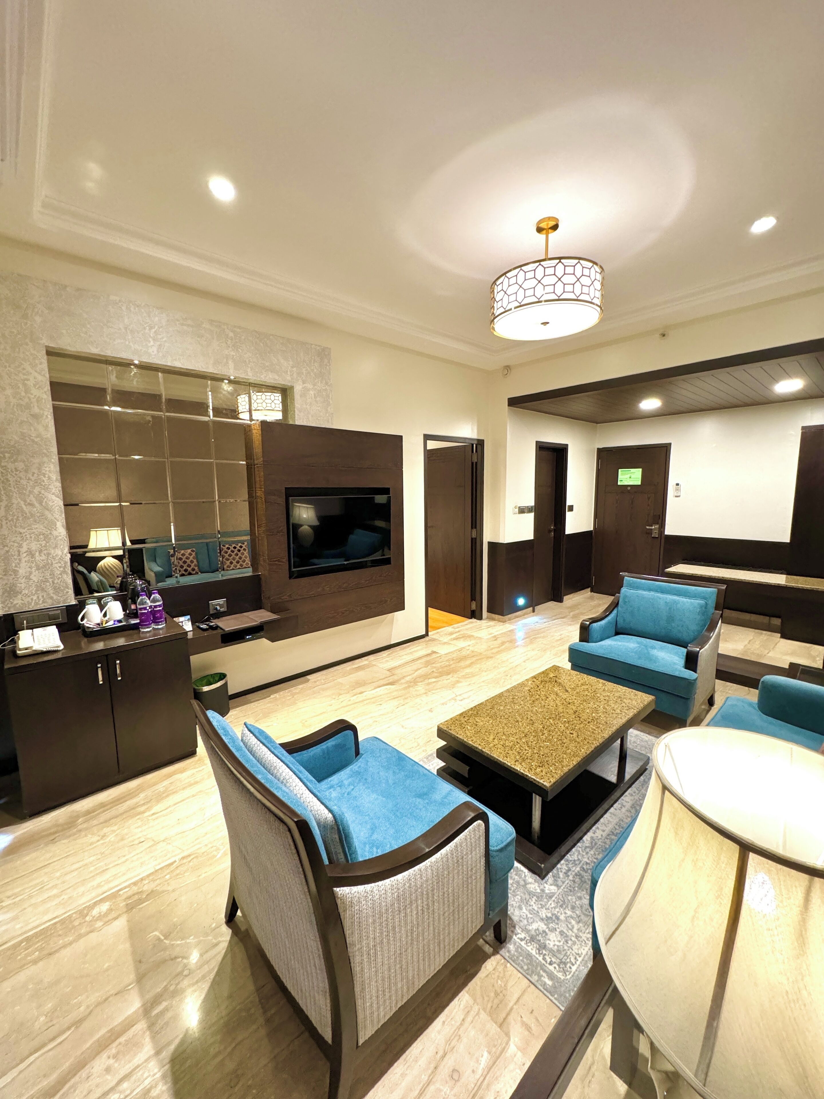 A modern hotel lobby with a seating area, a reception desk, a television, and a chandelier.