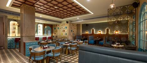 Een restaurant met een schaakbordvloer, ronde tafels en blauwe gestoffeerde zitbanken.