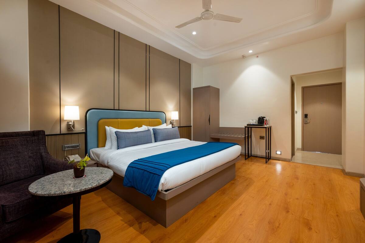 A hotel room with a bed, a small table with a plant, a sofa, a wardrobe, and a door.