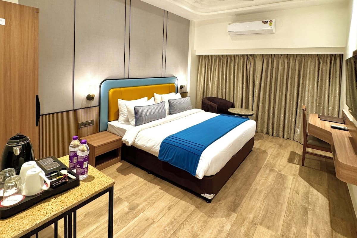 A hotel room with a bed, bedside table, desk, chair, and an air conditioning unit.