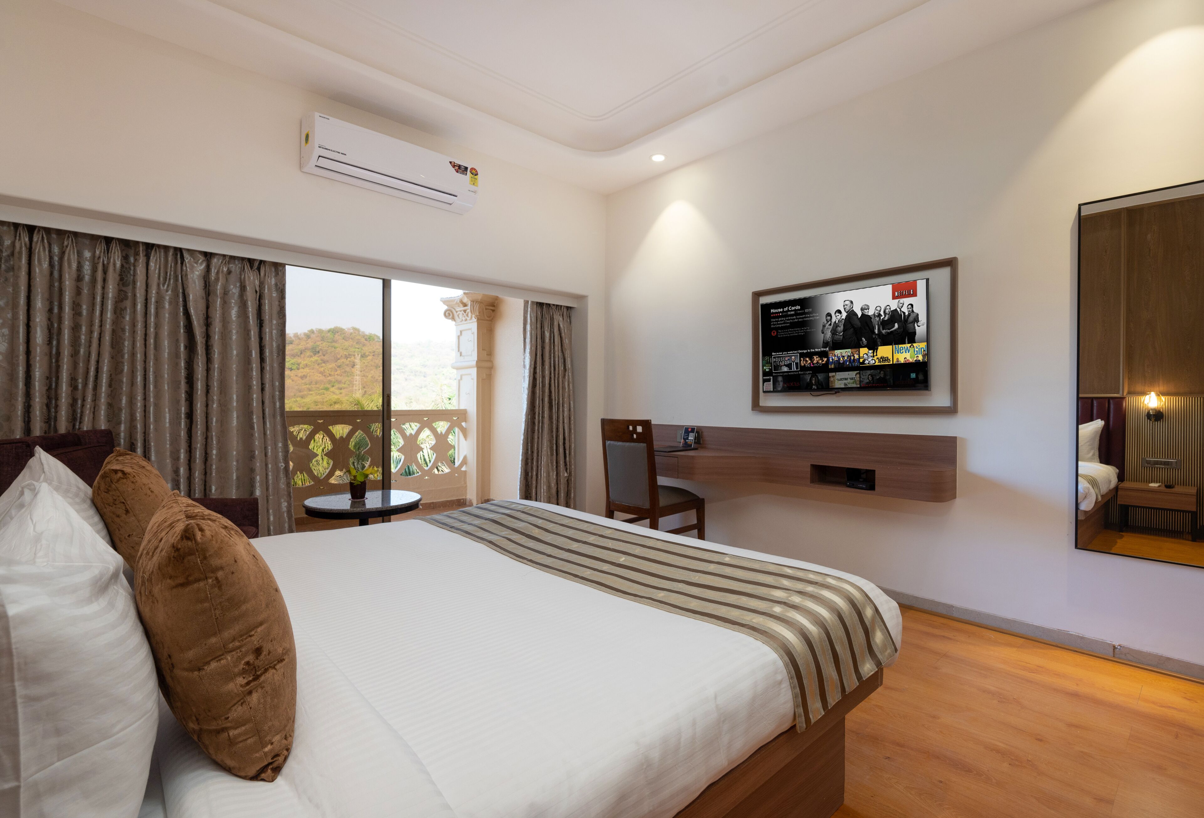 Habitación de hotel con una cama grande, un televisor en la pared, un escritorio y vistas al exterior.