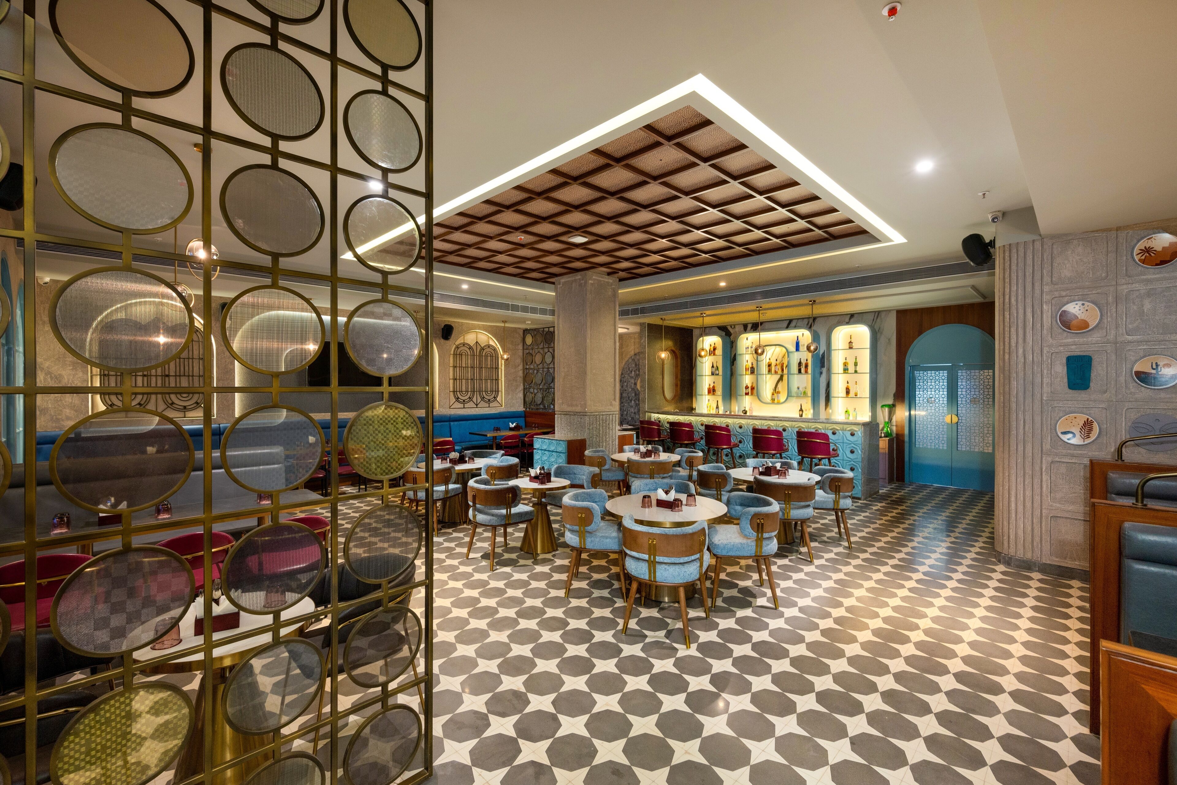 A restaurant with round tables and blue chairs, a patterned floor, and a ceiling with a grid design.