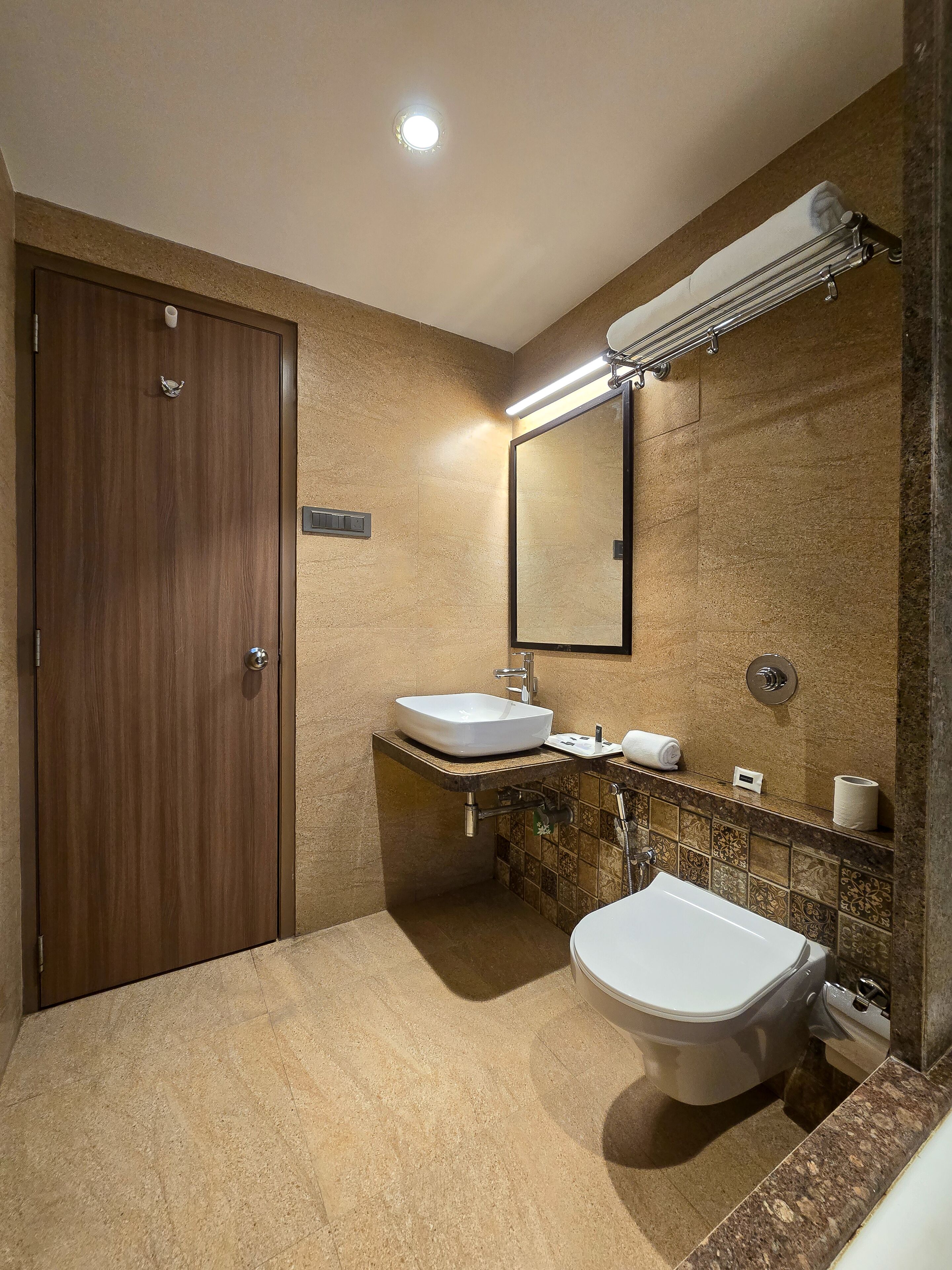 Un baño moderno con puerta de madera, dos lavamanos, un inodoro y un espejo.