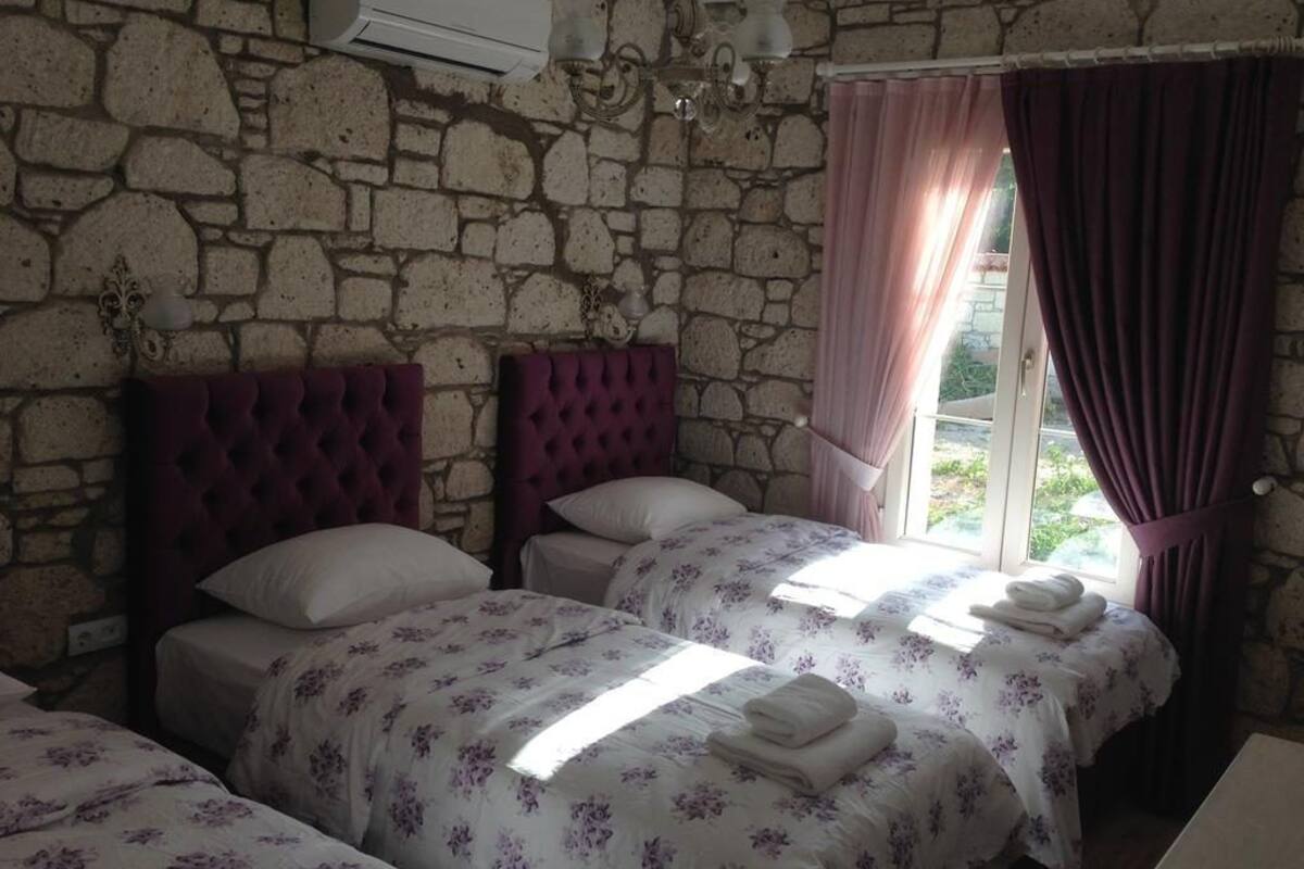 A room with two beds, stone walls, a chandelier, and a window with curtains.