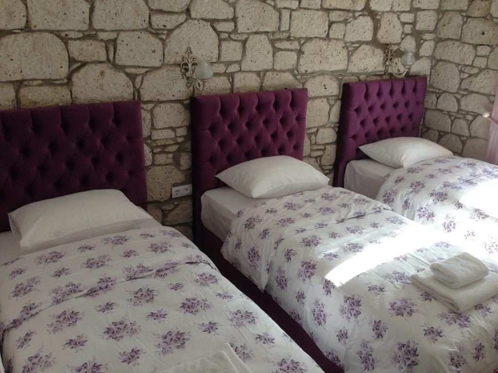 Habitación con tres camas frente a una pared de piedra, cada una con cabecero morado y ropa de cama floral.