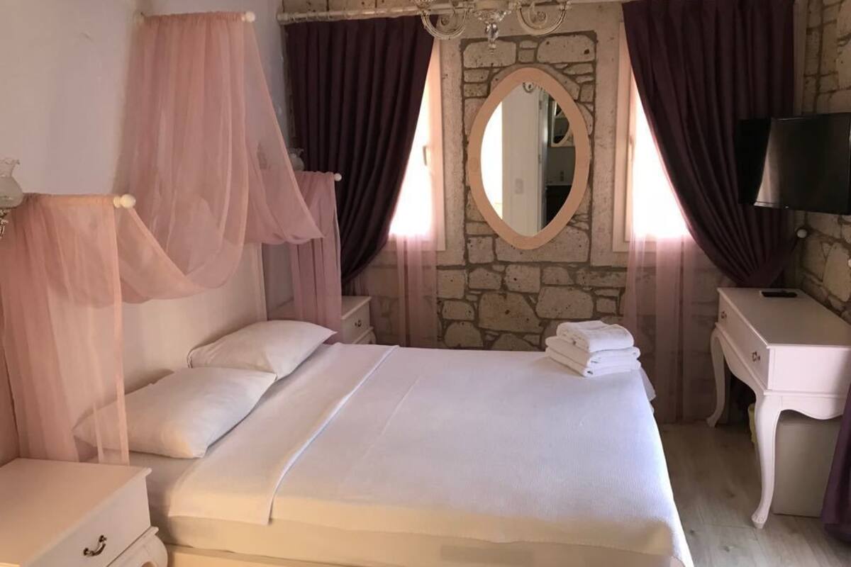 A bedroom with a large bed, a bedside table, a dresser, a mirror, and a chandelier.