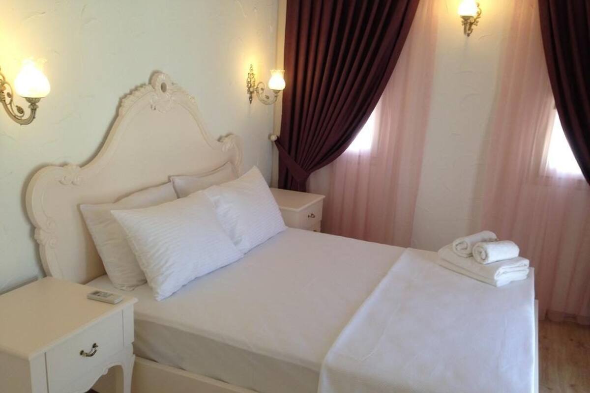 A neatly made bed with white linens, a bedside table with a lamp, and a window with curtains.