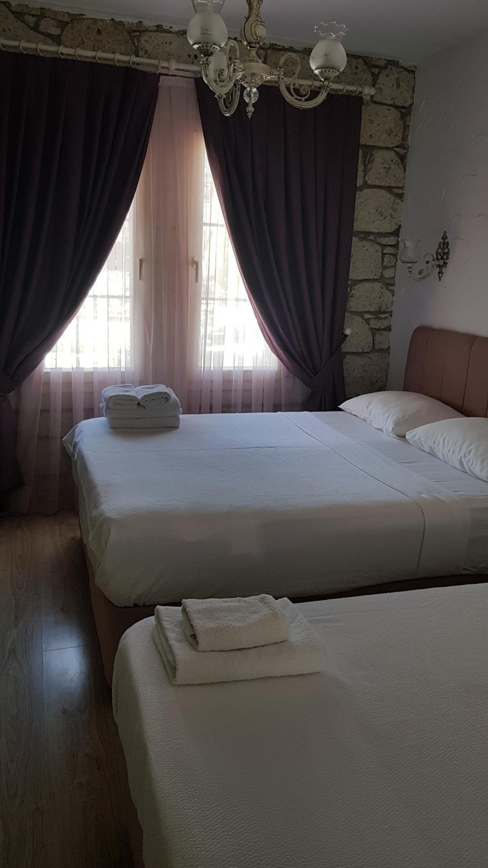 A hotel room with two beds, a stone wall, a chandelier, and a window with curtains.