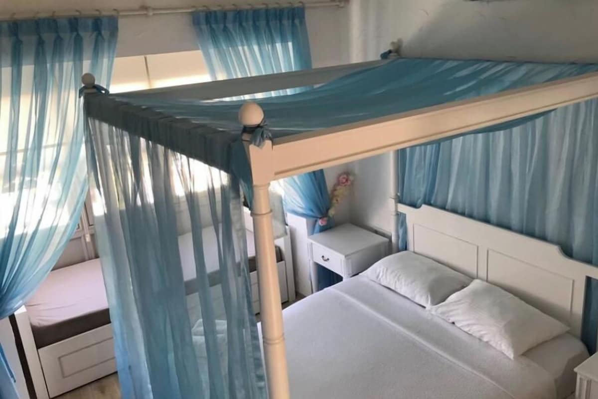 A bedroom with a canopy bed, a bedside table, and a nightstand.
