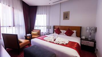 A hotel room with a large bed, a chair, a bedside table, and a nightstand.