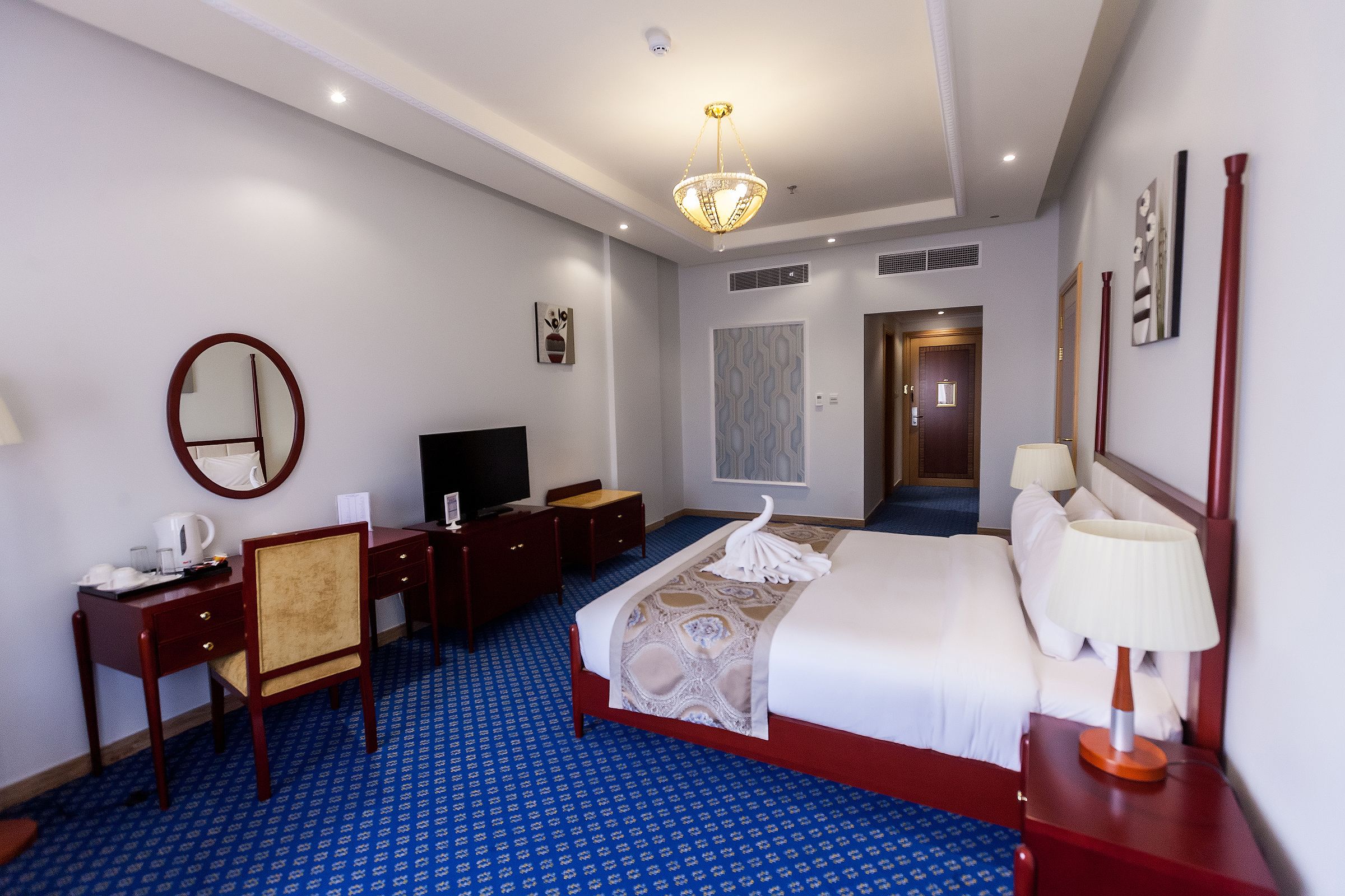 Habitación de hotel con cama, escritorio, silla, televisor y puerta de baño.