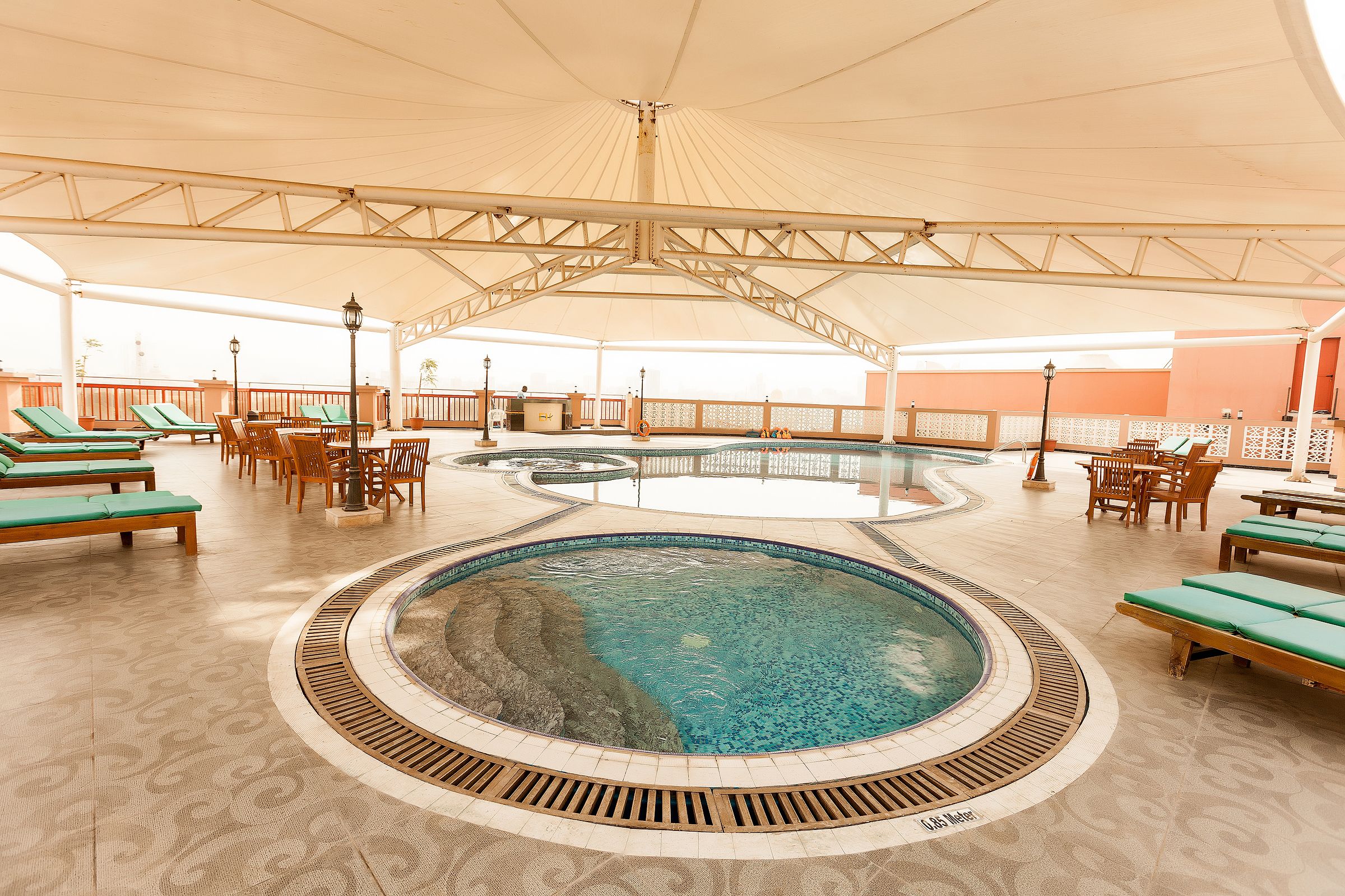 A covered swimming pool area with lounge chairs and tables, a central pool, and a tiled floor.