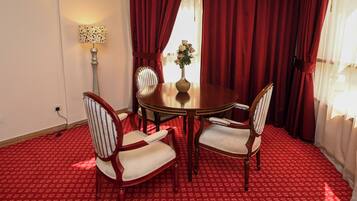 A dining area with a round table, four chairs, a vase with flowers, red curtains, and a lamp.