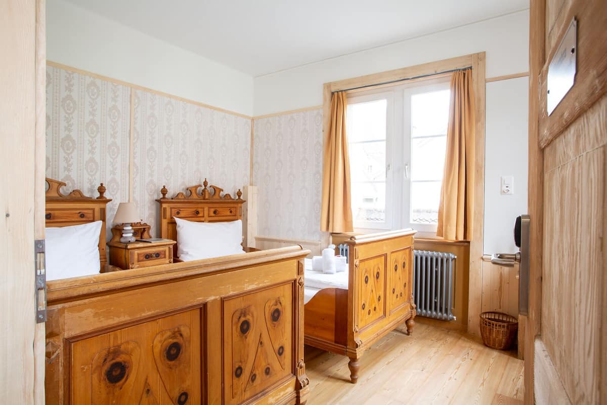 Een traditionele slaapkamer met een houten bed, nachtkastje, dressoir en een raam met gordijnen.
