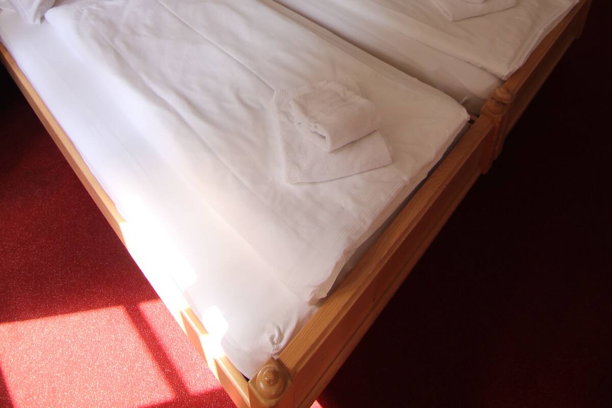 Een tweepersoonsbed met witte lakens, een houten hoofdbord en een vloerbedekking van rood tapijt.