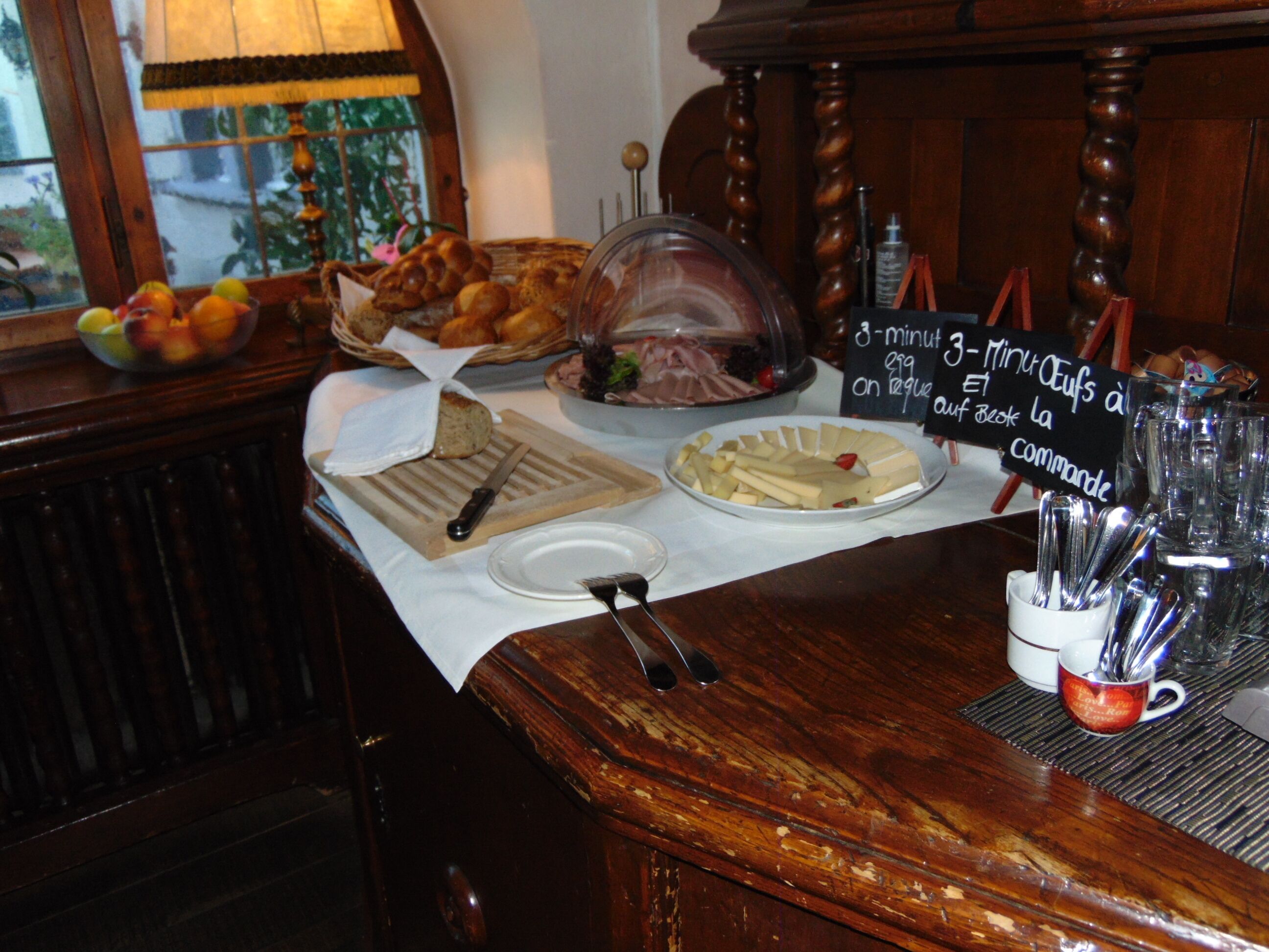 Un buffet de petit-déjeuner proposant du pain, des viennoiseries, du fromage, et un panneau indiquant qu’il est possible de demander des œufs cuits pendant 3 minutes.