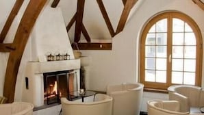 A cozy room with a fireplace, white leather chairs, and a large arched window. - Hotel Zunfthaus zur Rebleuten (Chur)